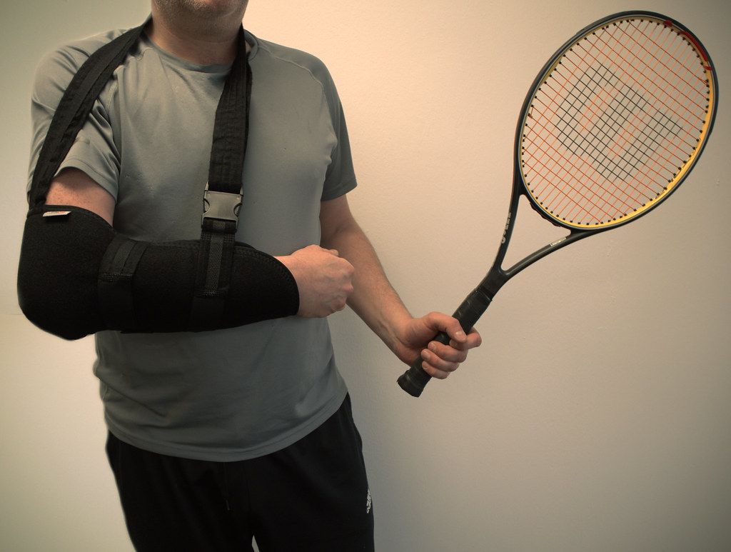 Tennis player with an arm in a sling holding a racquet