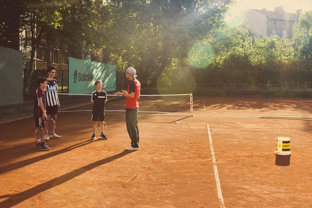 A coach working with young players on a clay court